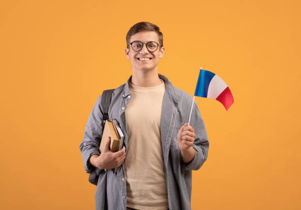European education, modern study or exchange student European education, modern study or exchange student. Young happy guy in glasses with backpack, notepads and small flag of France, isolated on orange background, copy space, studio shot Study Abroad Countries stock pictures, royalty-free photos & images