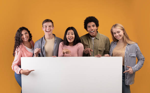 Group of friends laughing, sharing good and positive mood Group of friends laughing, sharing good and positive mood. Happy young multiracial students with open mouths hold banner with blank space, isolated on orange background, studio shot, panorama multi ethnic group college student group of people global communications stock pictures, royalty-free photos & images