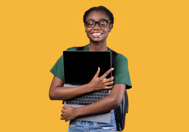 istock Happy Black Female Student Hugging Laptop Standing Over Yellow Background 1291773258