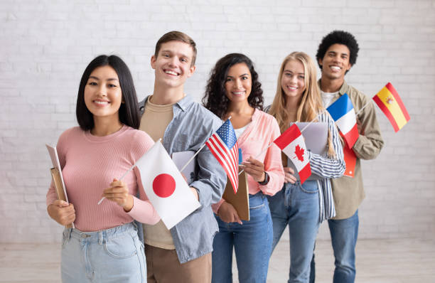 istock International multi-ethnic student exchange. Cheerful young people with devices and books look at camera 1291773268