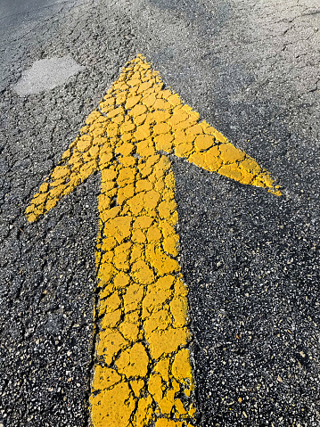 close up shot of yellow arrow sign on cracked asphalt road