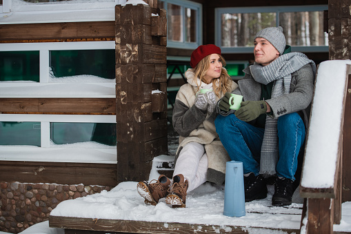 After spending a day off in the woods in winter, a young couple basks in a summer house and drinks a hot drink from mugs.