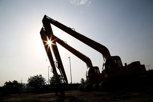 Silhouette of a large crawler excavator working on the sea embankment against the backdrop of a stunning sunset. Digging the ground for the foundation and construction of a new building.