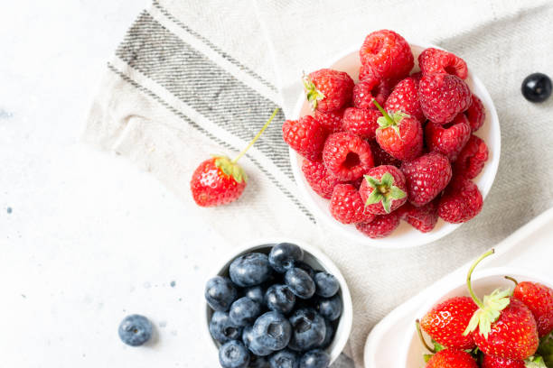 istock Ripe berries. Different berries in white ceramic bowls on a light table. Strawberries, raspberries and blueberries in plates 1291786004