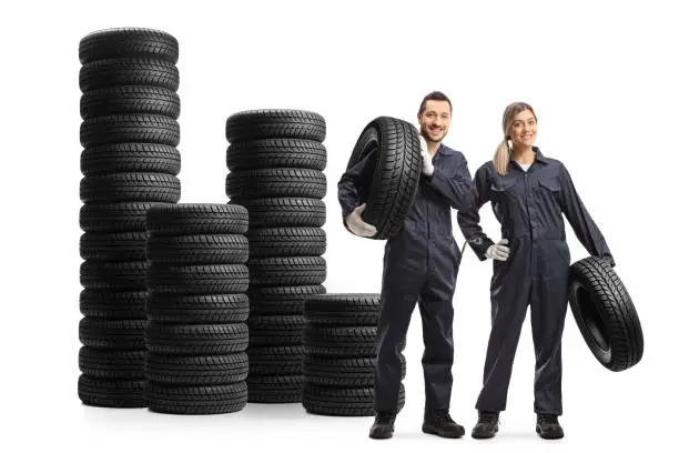 Male and female auto mechanic workers with piles of vehicle tires isolated on white background
