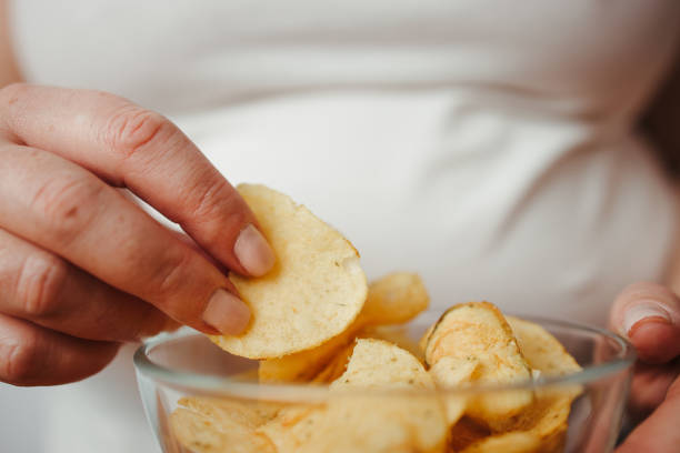 istock Overweight woman eating chips from bowl, close up 1291788903
