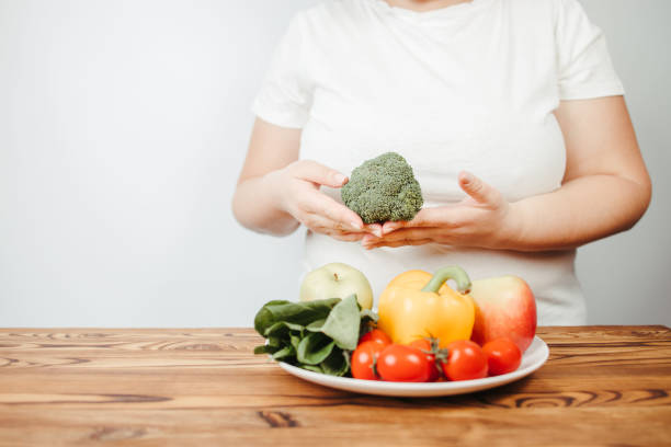 istock Fat woman snacking with fruits and vegetables 1291789073