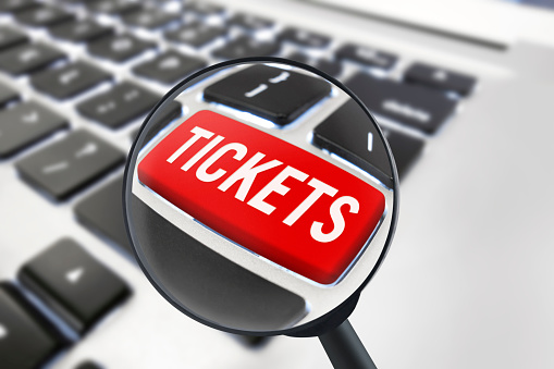 hand clicking on a “Tickets” button with magnifying glass on a keyboard