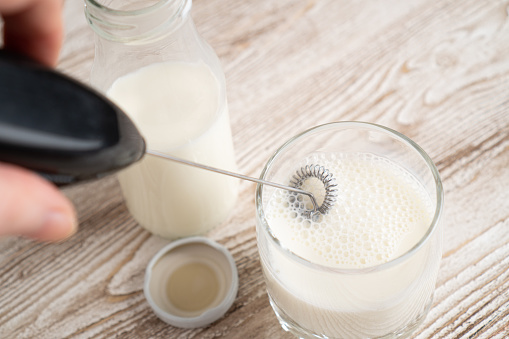 Mezclar la leche en vidrio con espumador de leche. Hacer leche espumosa con espuma. Mezclador de mano de leche. photo
