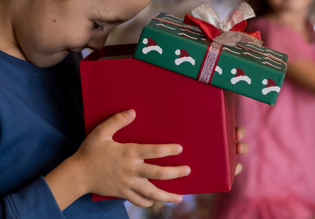 close up of little boy holding present gift box and looking, peeking inside. merry christmas and happy holidays - christmas child little boys peeking imagens e fotografias de stock