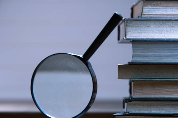 istock Searching... stack of book  with magnifier glass, side view 1291793200