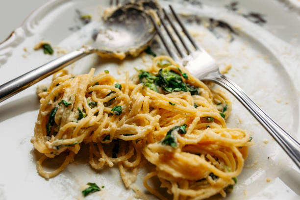 istock Spaghetti in creamy spinach sauce with cheese, on a messy floral plate with silver fork and spoon, half eaten, close up 1291793899