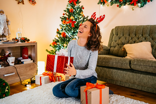 Beautiful young smiling woman opening Christmas gifts at home.