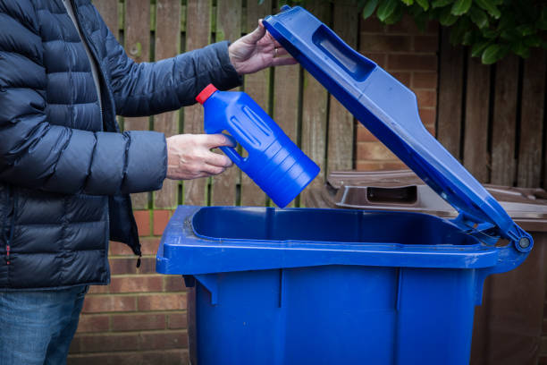 A man recycling plastic bottles in a blue kerb side recycling bin