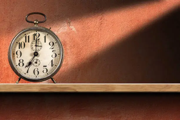 Photo of Old Alarm Clock above a wooden shelf on red wall