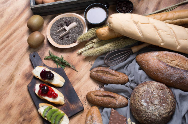 istock Breakfast and baked bread concept. Fresh fragrant bread and egg on wooden table. Fresh bread and coffee and wheat on wood black background. Kiwi and chocolate. 1291803523