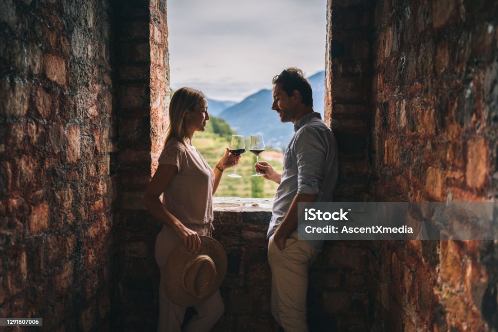 Couple enjoy some red wine in ancient Italian castle They look outside window toward vineyard and cheers in celebration Travel Stock Photo