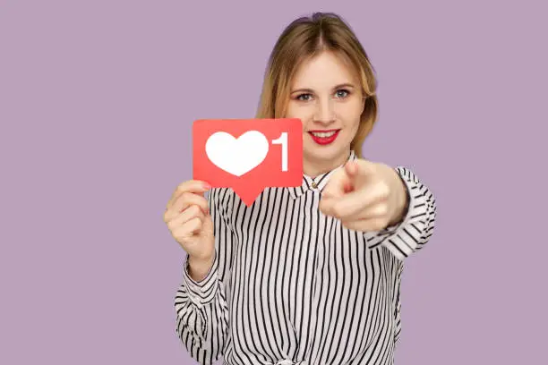 Photo of Hey you, put like to content! Pretty woman with red lips in glamour striped blouse holding social media heart icon