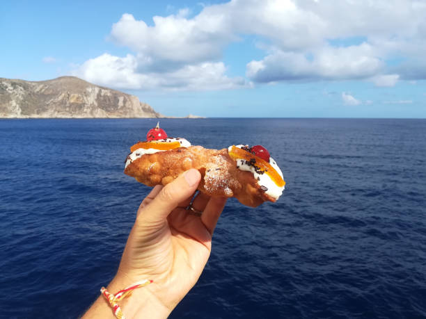 Hand with sicilian cannolo with the sea and Egadi Island in the background Hand with sicilian cannolo with the sea and Egadi Island in the background egadi islands photos stock pictures, royalty-free photos & images