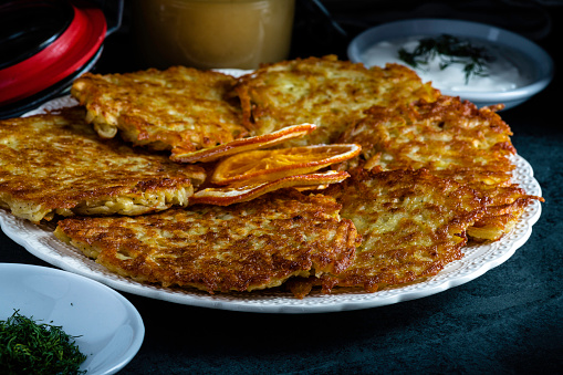 Potato latkes served with traditional accompaniments of sour cream, applesauce, and dill. Garnished with dried orange slices.