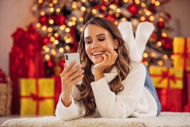 istock Beautiful woman using smart phone near Christmas tree 1291815808