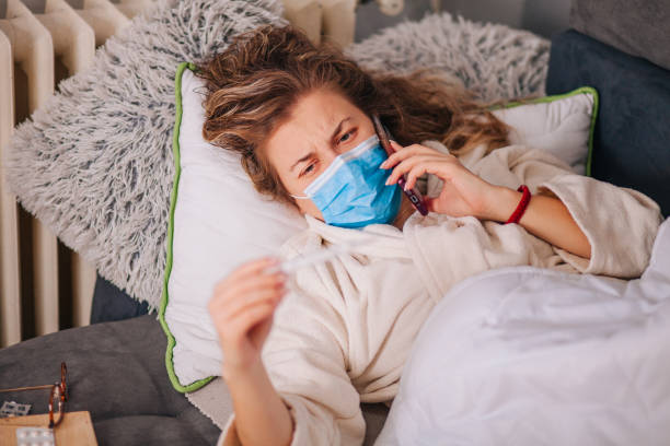 istock Sick woman with face protective mask using mobile phone and lying in bed 1291817153