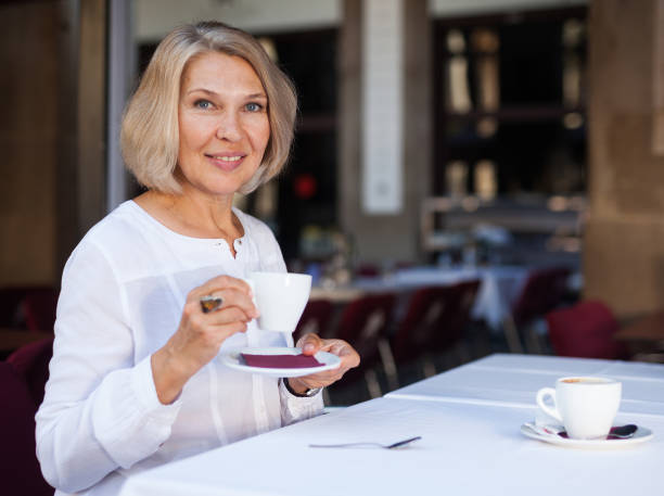 позитивная зрелая женщина 50 лет обедает с кофе в кафе - 60 64 years стоковые фото и изображения