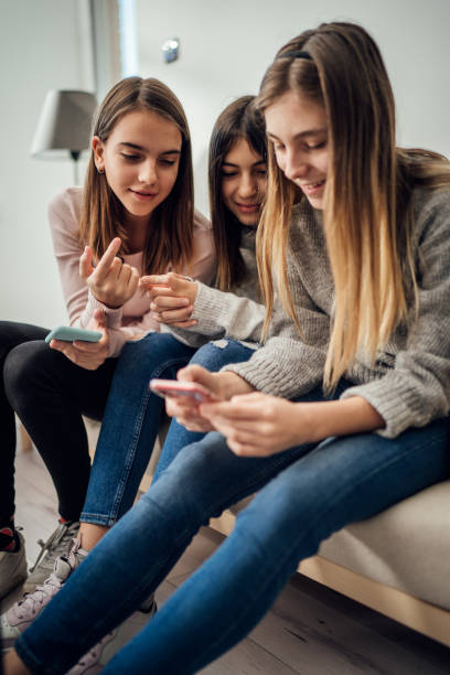 tre ragazze sedute in salotto e che usano un telefono cellulare insieme - 12 15 months foto e immagini stock