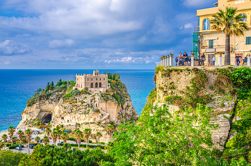 Tropea, Italy - May 8, 2018: people tourists on observation deck view platform Belvedere Piazza del Cannone are looking at Monastery Sanctuary church Santa Maria dell Isola on top of rock