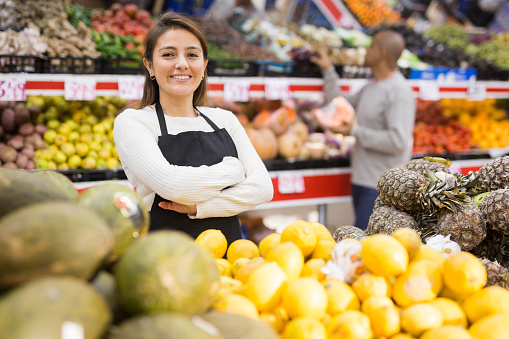 Supermarket woman worker in  black apron putting melons in his department