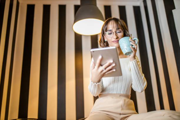 istock Beautiful young woman using digital tablet, reading magazine and drinking coffee at home 1291826220