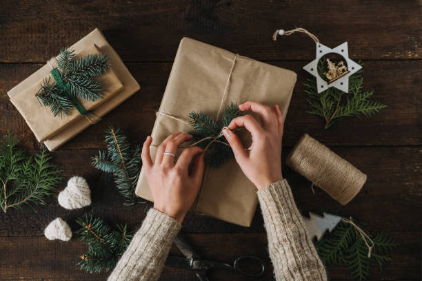istock Christmas wrapping idea, xmas wrapping workspace. Female hands wrap gift box in kraft recycled paper. Eco-Friendly, Sustainable, zero waste, natural color Christmas gift boxes on wooden background. 1291832064