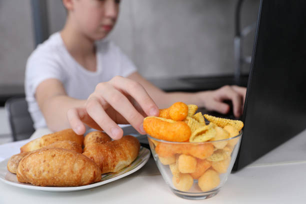Boy working using computer and eating fast food and snacks. Unhealthy Lifestyle. Covid 19 Homeschool stock photo