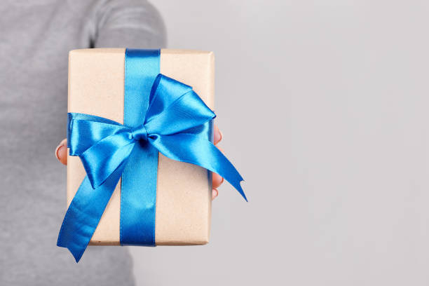 istock Hand with giftbox with blue ribbon on grey background. 1291835554
