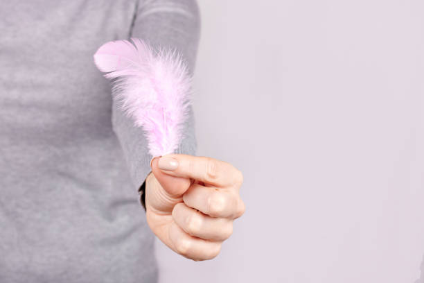 istock Hand with purple feather on grey background. 1291835593