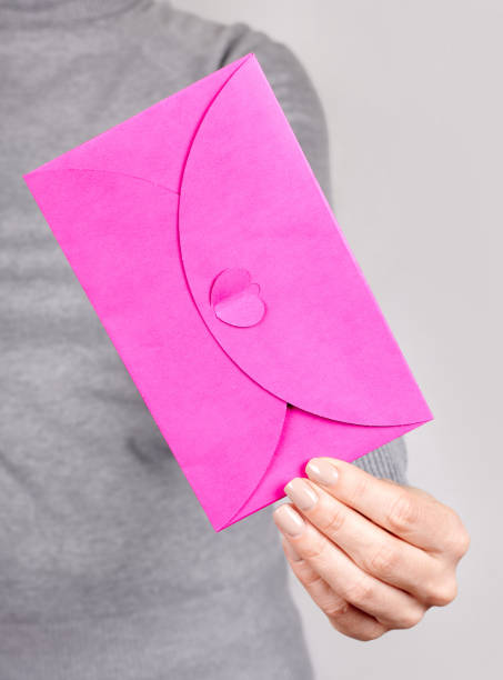 istock Hand with pink paper envelope on grey background. 1291835617