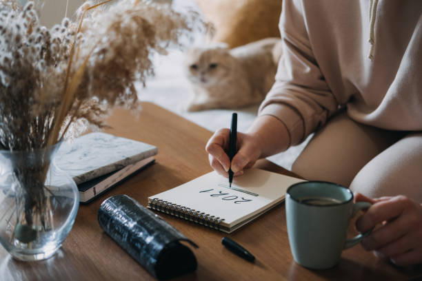 2021 goals, new year resolution, planning. Woman writing in Notebook with text 2021 loading on the table in apartments with cat. Notepad list concept, hand writting text 2021 and loading scale