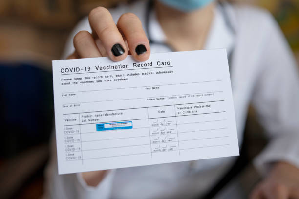 Doctor holding COVID-19 Vaccination Record Card. Close up of unrecognizable female doctor holding a COVID-19 Vaccination record card. anti vaccination photos stock pictures, royalty-free photos & images