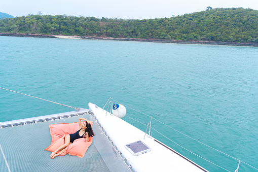 Asian girl in nice black bikini lay down relaxing on bean bag in part of cruise yacht with background of blue water sea and green island. Concept luxury travel with nature of sea.