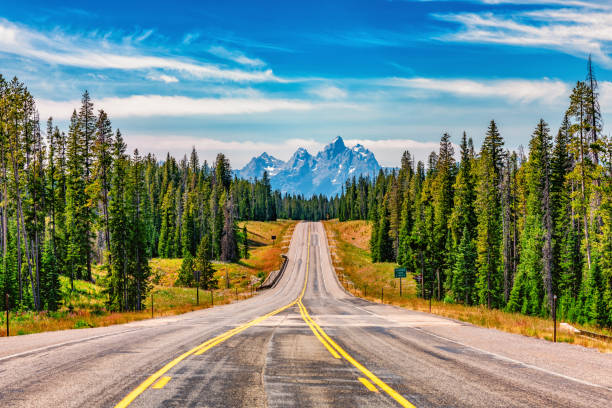 Road into the Tetons A mountain highway through the forest toward Grand Teton National Park, Wyoming with the peaks of the Tetons in the background. teton range photos stock pictures, royalty-free photos & images