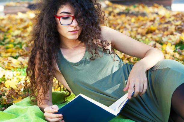 istock Young woman reading a book in the park 1291850035