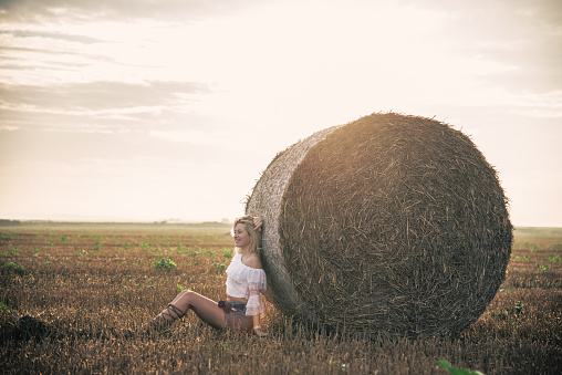 Beautiful young woman near hay bale in Summer in field
