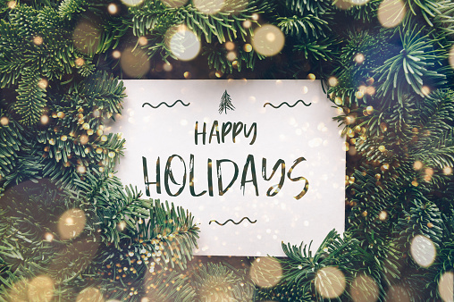 Happy holidays text, card concept. Holiday background with white card in the middle of evergreen tree branches with lights, christmas and festive season idea, minimalistic design