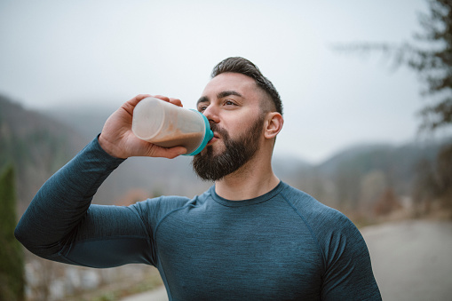 Beard man athlete drinking protein after outdoor workout.
