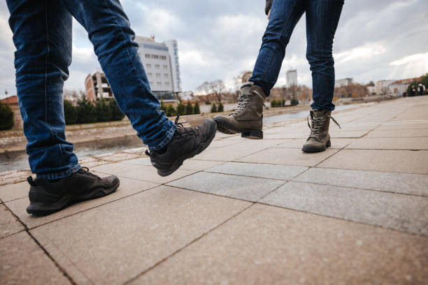 Two friends meet, instead of greeting each other with a hug or handshake, they touch each other with their feet, close-up of foot bump concept