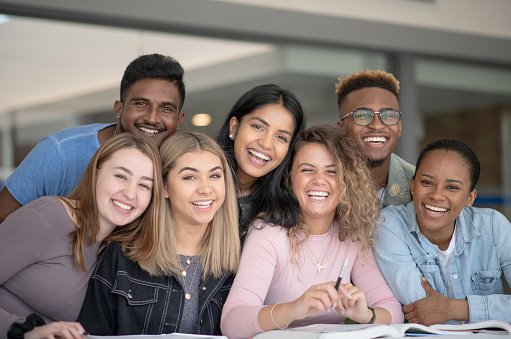 A group of multi ethnic university students all smiling together for the camera. They appear to be happy to be friends with each other at university.