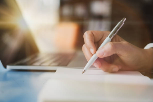 istock Woman hand writing down in small white memo notebook for take a note not to forget or to do list plan for future. 1291872154