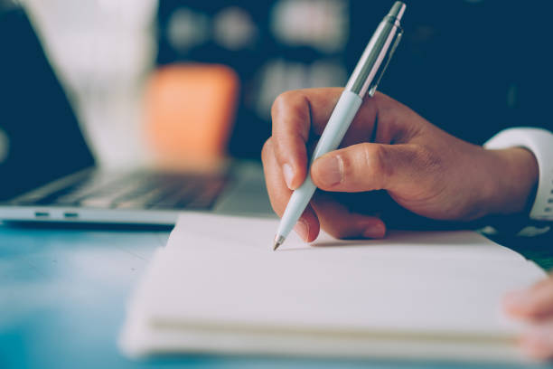 istock Woman hand writing down in small white memo notebook for take a note not to forget or to do list plan for future. 1291872155