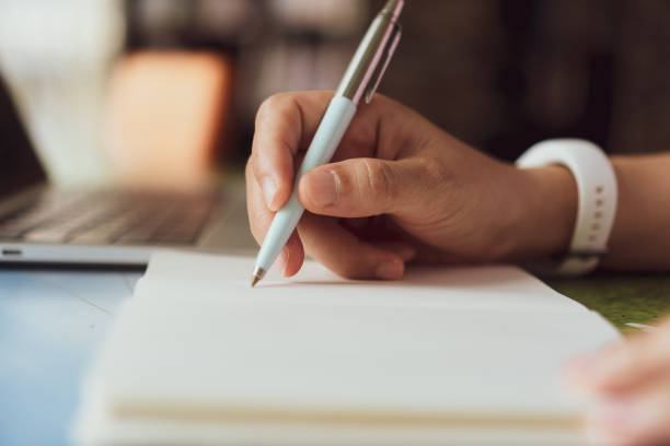 istock Woman hand writing down in small white memo notebook for take a note not to forget or to do list plan for future. 1291872162