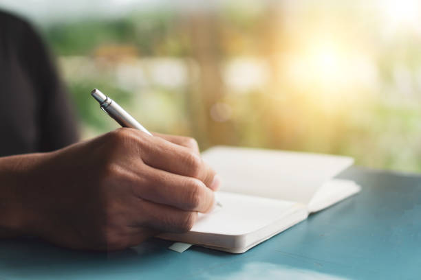 istock Woman hand writing down in small white memo notebook for take a note not to forget or to do list plan for future. 1291872165